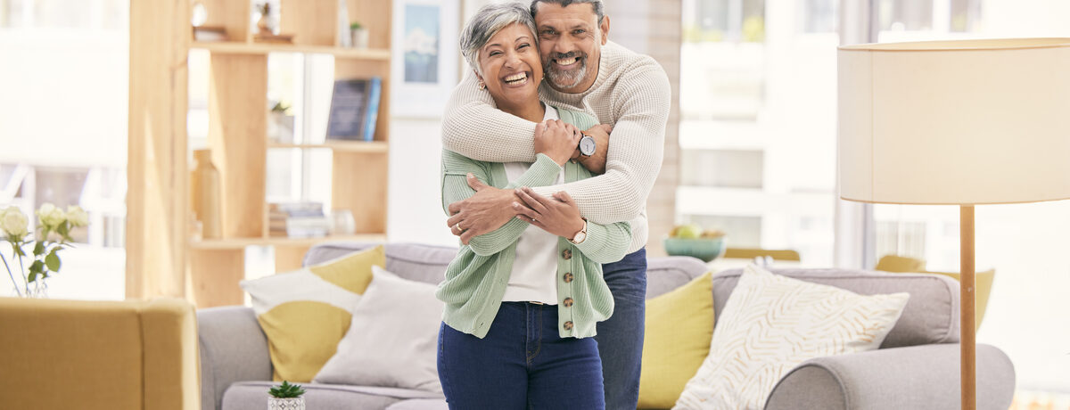 A man with his arms around a smiling woman in a bright living room