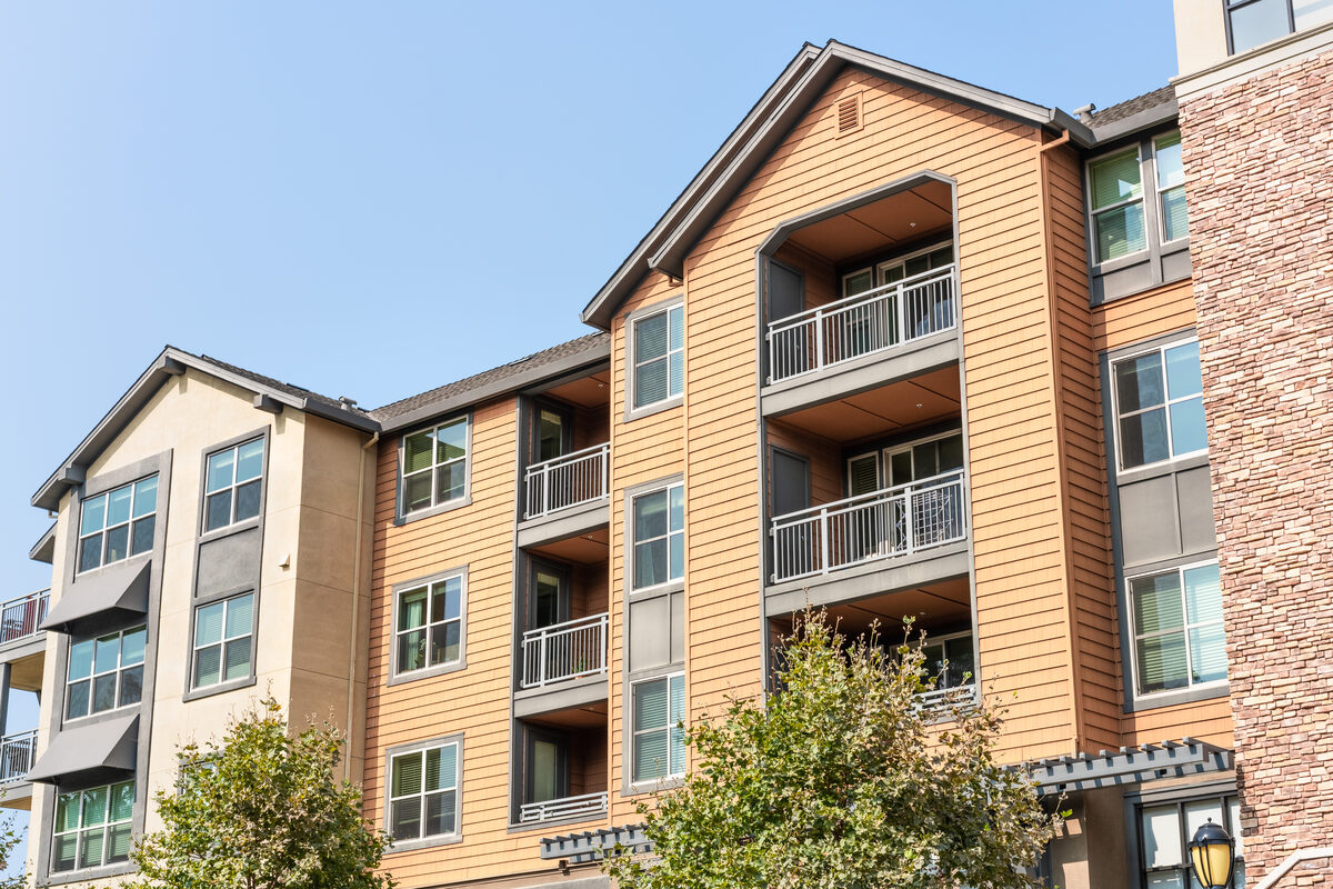A four-story apartment building with balconies and warm timber siding under a clear sky