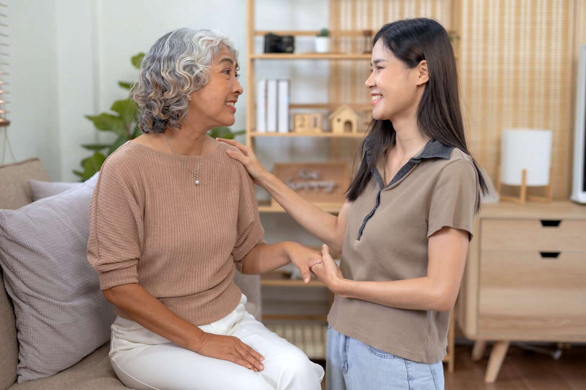 An older woman standing in her living room with a younger woman beside her, a hand resting on her shoulder
