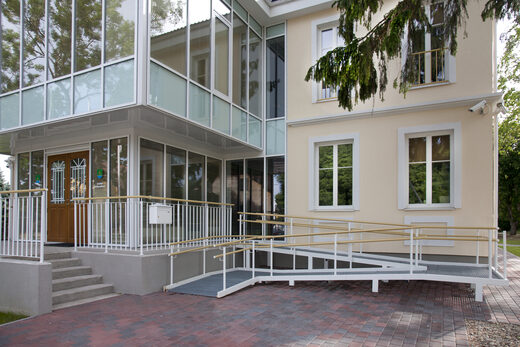 A building entrance with a long wheelchair ramp and metal handrails beside a short flight of steps